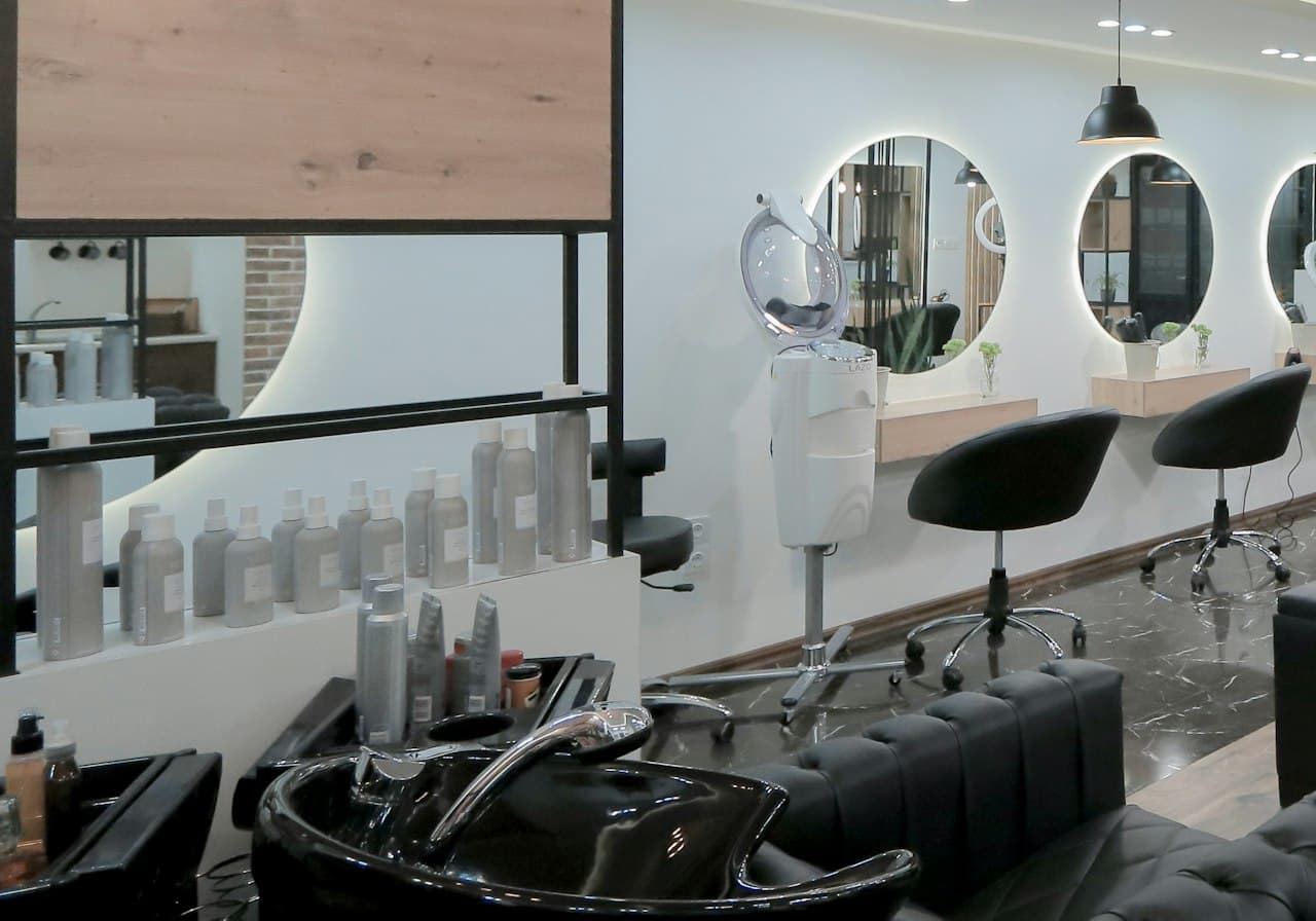 Symbolbild: Heller Salonbereich mit hinterleuchteten Spiegeln und schwarzen Stühlen.
